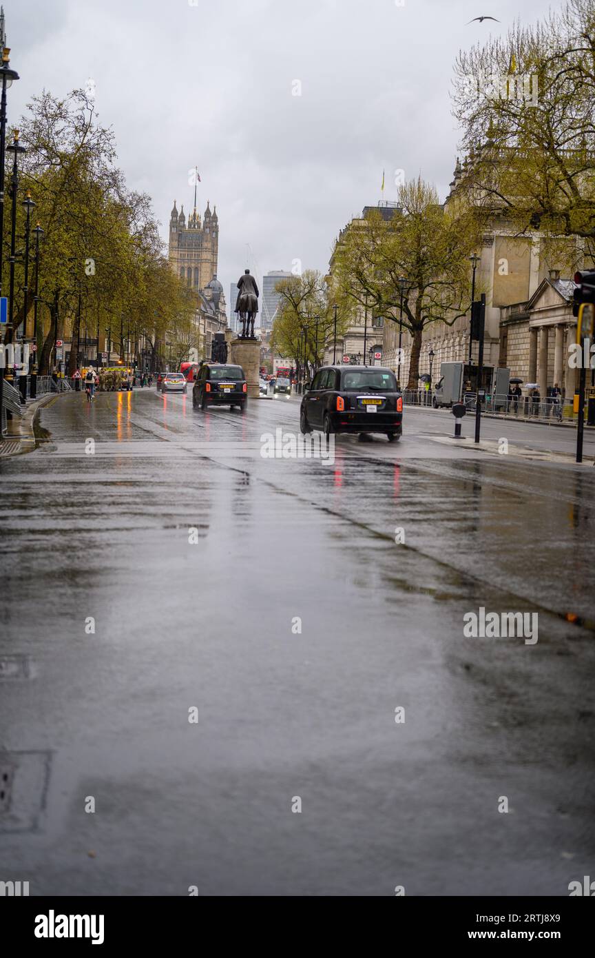 LONDRES - 24 avril 2023 : des taxis noirs naviguent à Whitehall par temps de pluie, avec les chambres du Parlement formant un décor majestueux. Banque D'Images