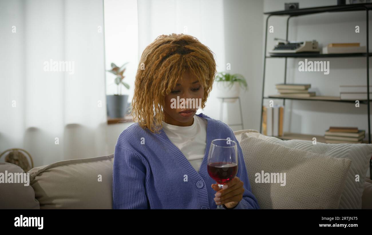 Afro-américaine pensive femme ethnique pensée pensée intriguée fille triste bouleversée femelle solitaire penser à la maison canapé avec du vin rouge mettre du verre sur Banque D'Images