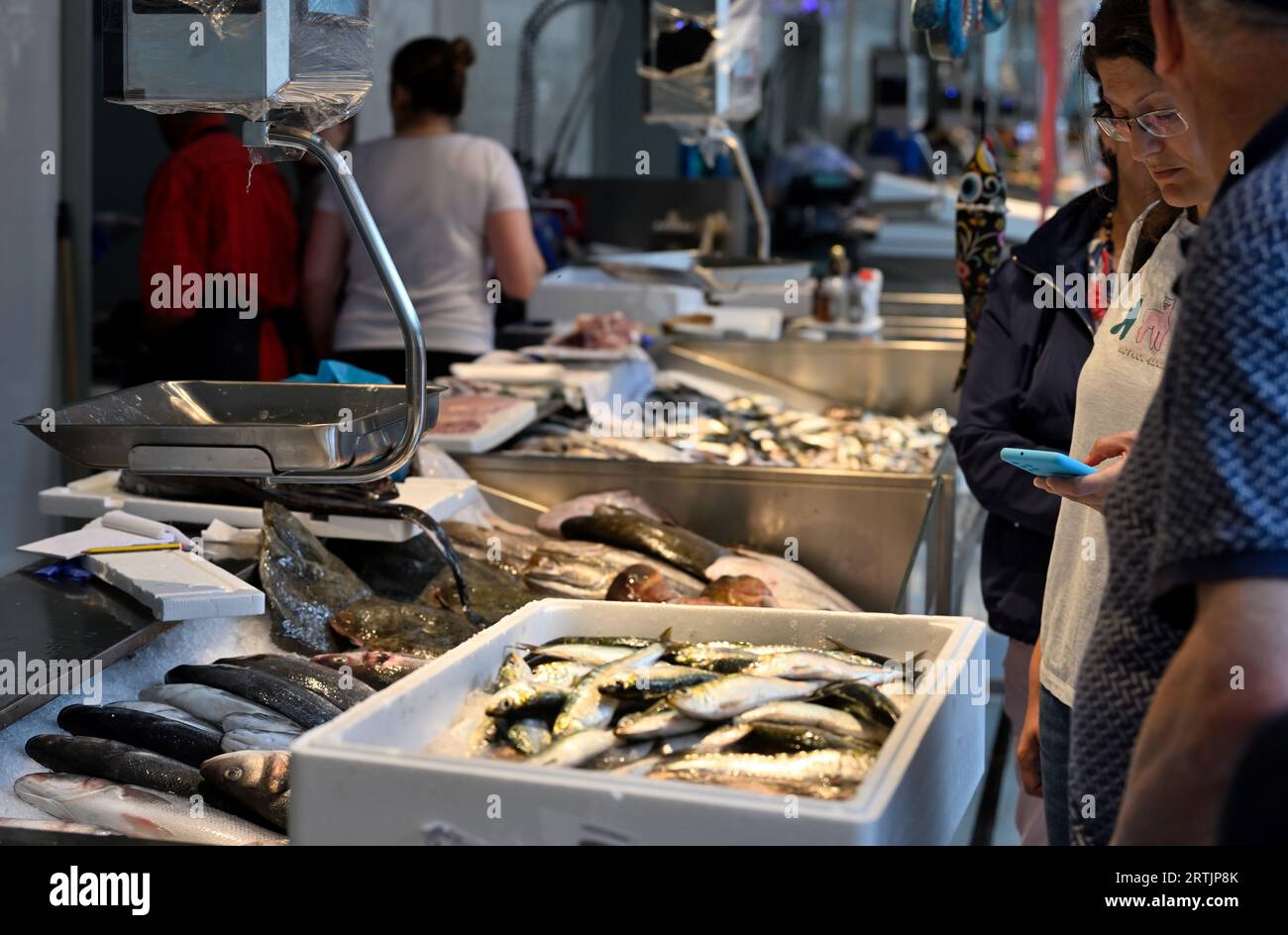 Femme debout vérifiant son téléphone debout attendant à l'intérieur du marché historique à deux niveaux, Mercado do Bolhão, étal de poisson frais Banque D'Images