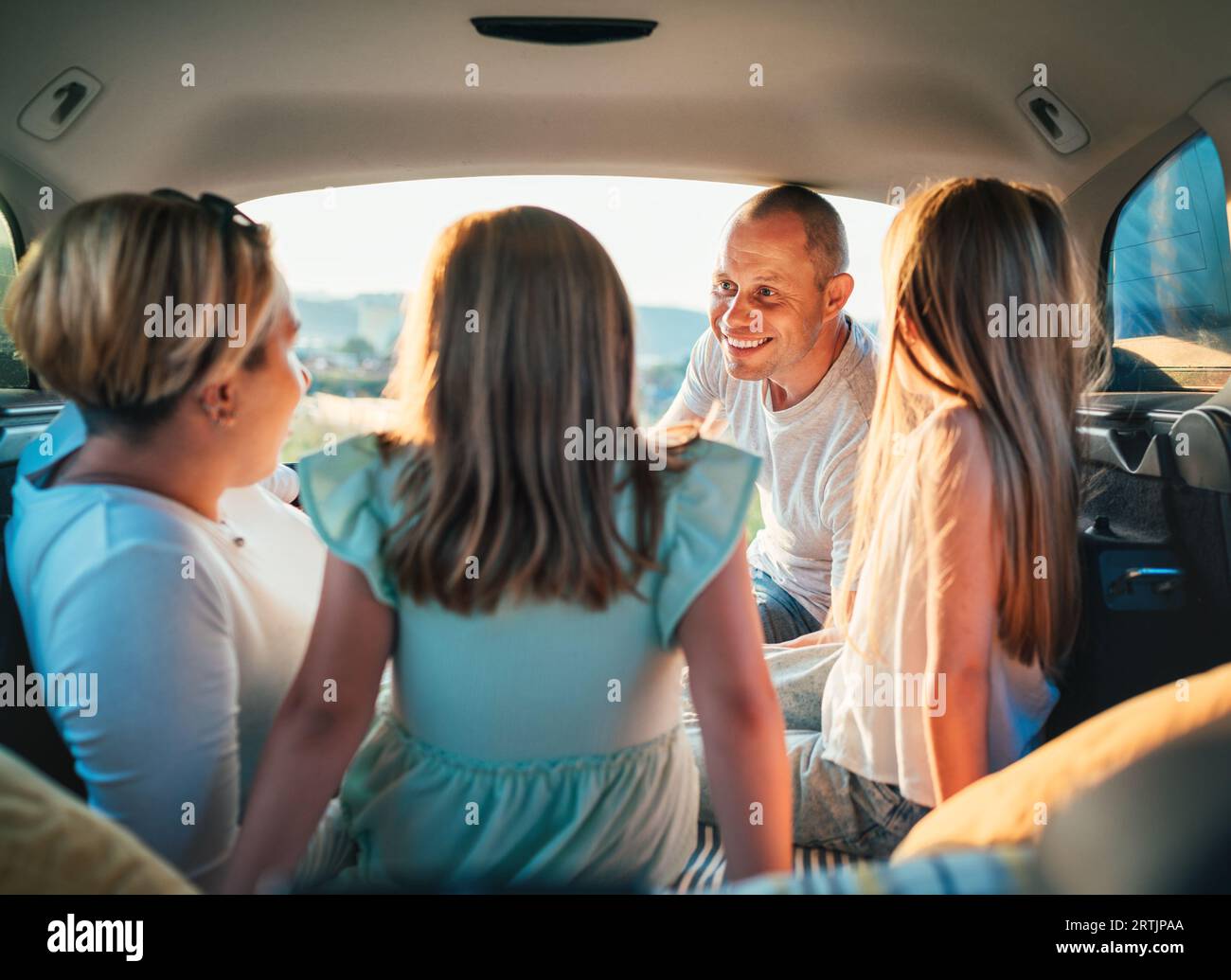 Heureux jeune couple avec deux filles à l'intérieur du coffre de la voiture pendant auto trop. Ils sourient, rient et bavardent. Portrait de père souriant heureux Banque D'Images