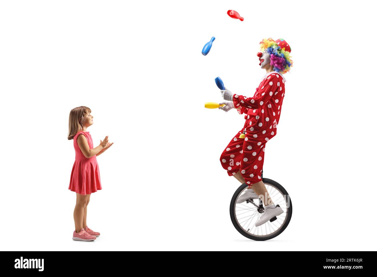 Petite fille applaudissant et regardant un clown chevauchant un monocycle et jonglant isolé sur fond blanc Banque D'Images