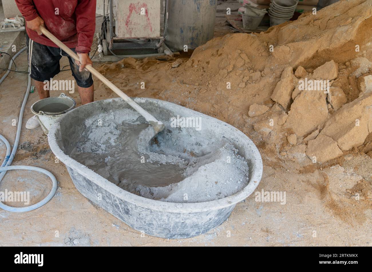 Travailleur mélanger manuellement la poudre de ciment sur le chantier de construction, en utilisant une houe pour mélanger la poudre de ciment, le sable, les pierres dans le bassin pour mélanger le ciment. Banque D'Images