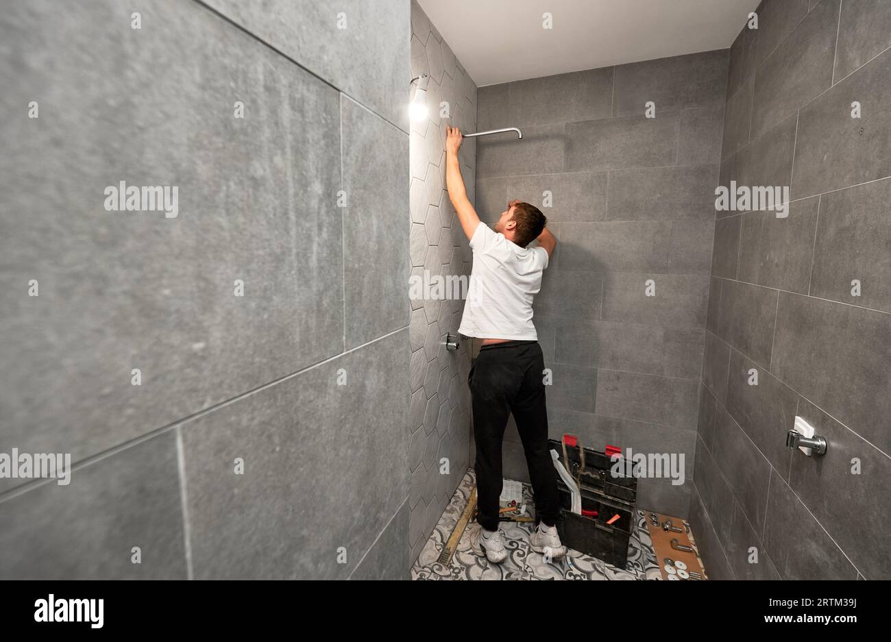 Plombier mâle fixant la pomme de douche de salle de bains tout en travaillant sur la rénovation de salle de bains. Vue arrière du travailleur de l'homme installant la pomme de douche de bain à haute pression à la maison. Banque D'Images