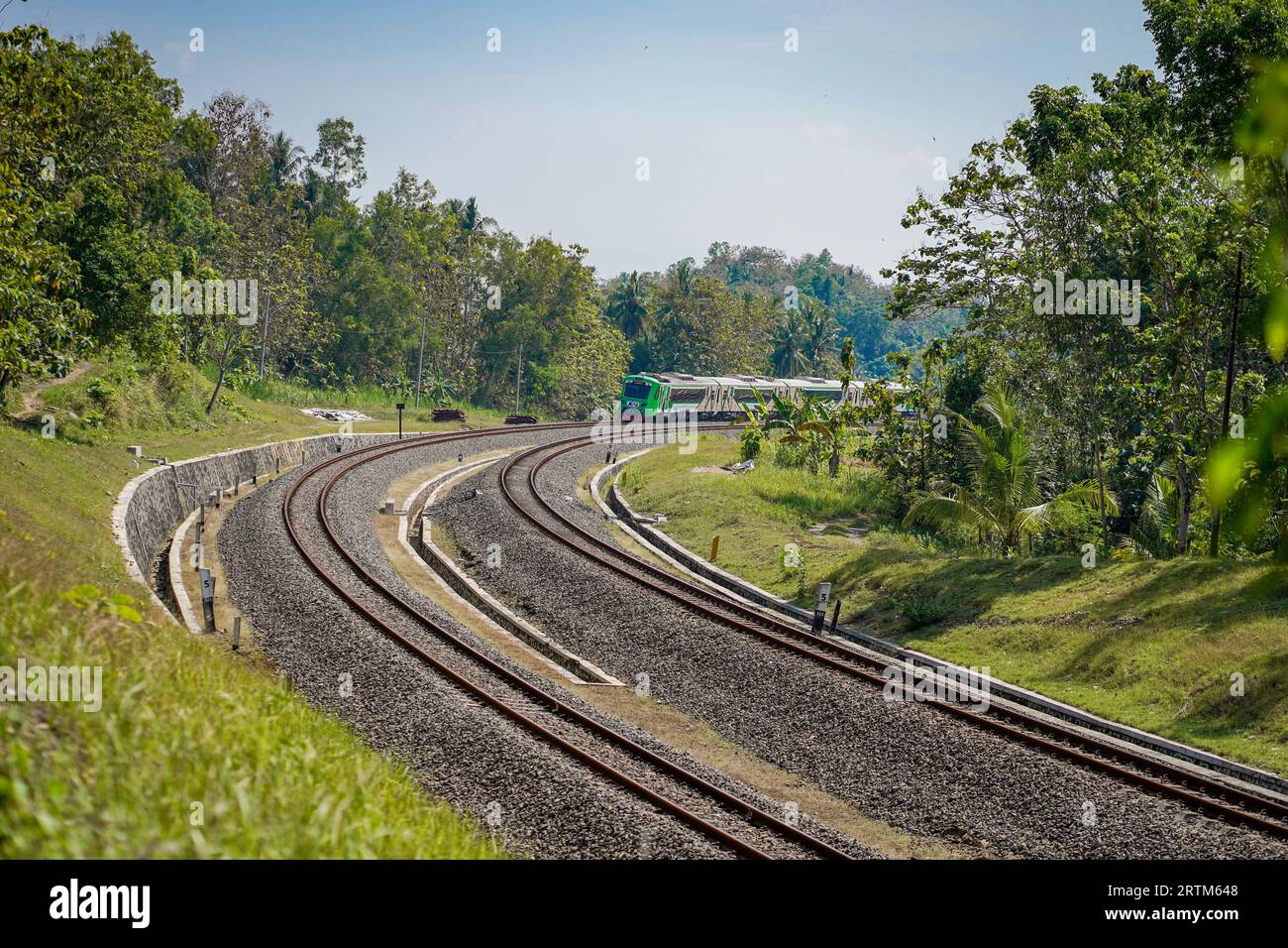 Un train commercial qui circule sur une ligne à 2 voies avec des vues à gauche et à droite de la forêt dense pendant la journée. : Kulon Progo, Indonésie - 07 août 2021 Banque D'Images