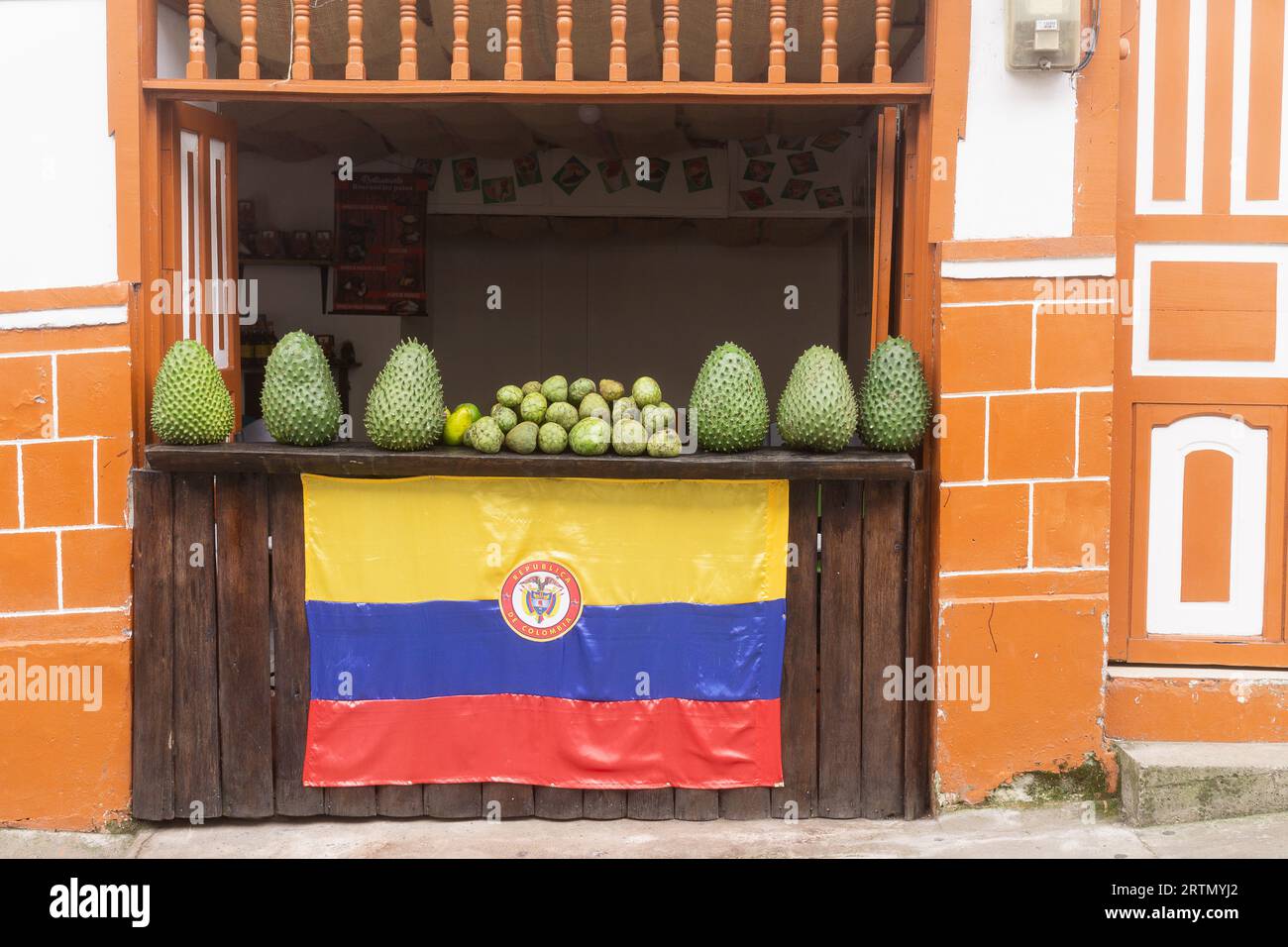 Grands fruits de corossol (guanábana) exposés dans une devanture traditionnelle ornée d'un drapeau colombien à Filandia, Quindío, Colombie. Banque D'Images