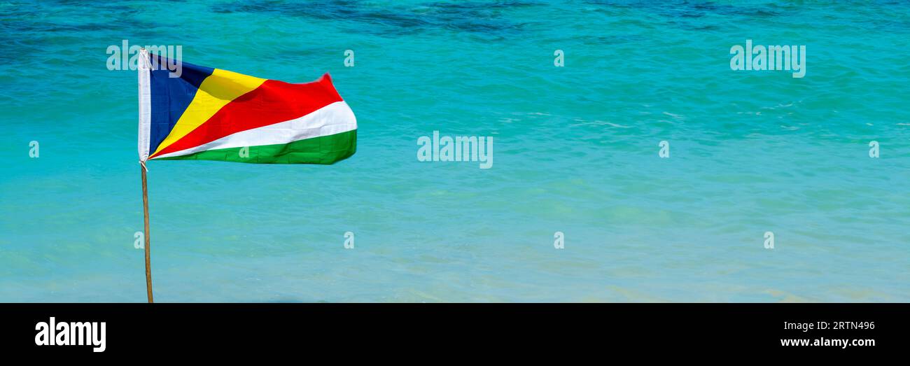 Drapeau des Seychelles sur une plage, fond panoramique d'eau turquoise avec espace de copie, bannière web de voyage des Seychelles Banque D'Images