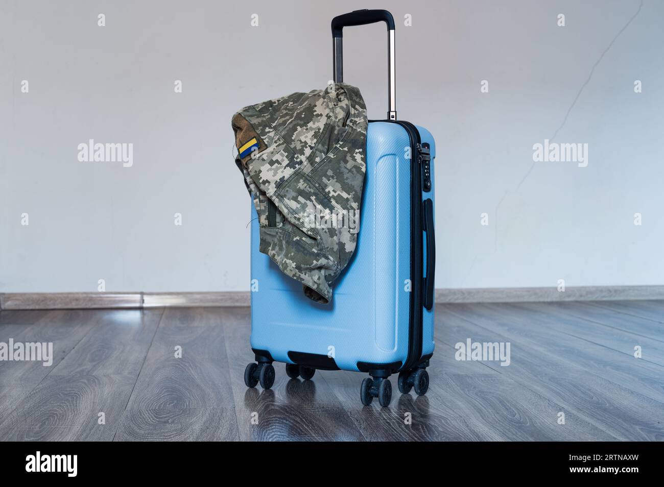 La valise bleue de voyage se tient sur le plancher en bois avec une veste uniforme de pixel militaire ukrainienne dessus Banque D'Images