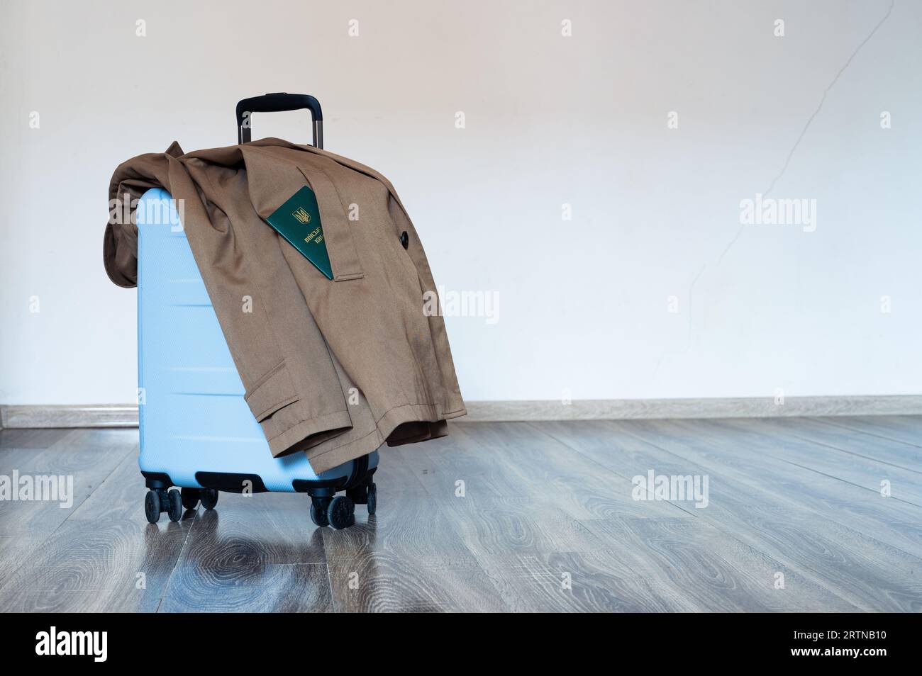 Traduction : 'ID militaire'. Valise bleue de voyage se tient sur le plancher en bois avec manteau. Doc vert militaire sortant de la poche Banque D'Images