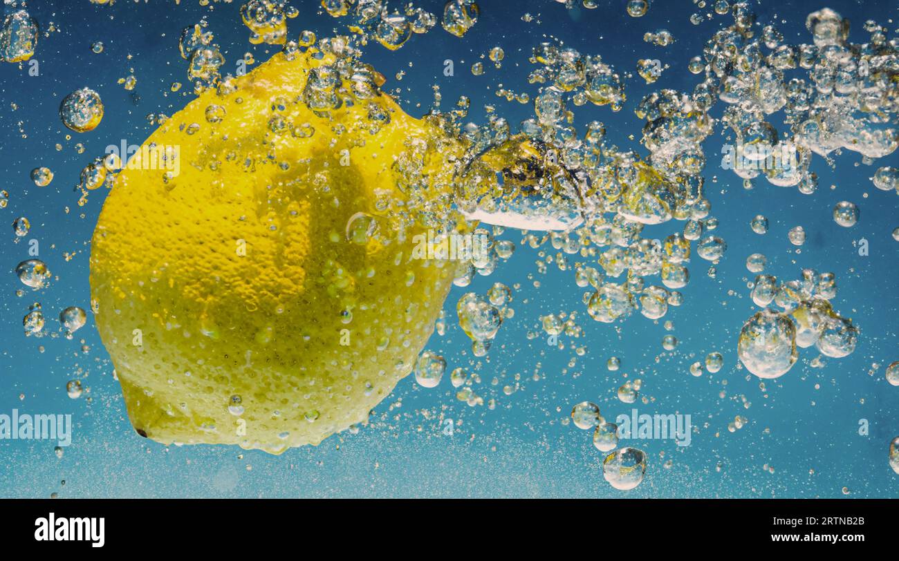 Tranche de citron sous-marine dans de l'eau gazeuse ou de la limonade avec des bulles. Cocktail rafraîchissant soda tonique pétillant. Gros plan de citrons et de glaçons en verre. Lime i. Banque D'Images