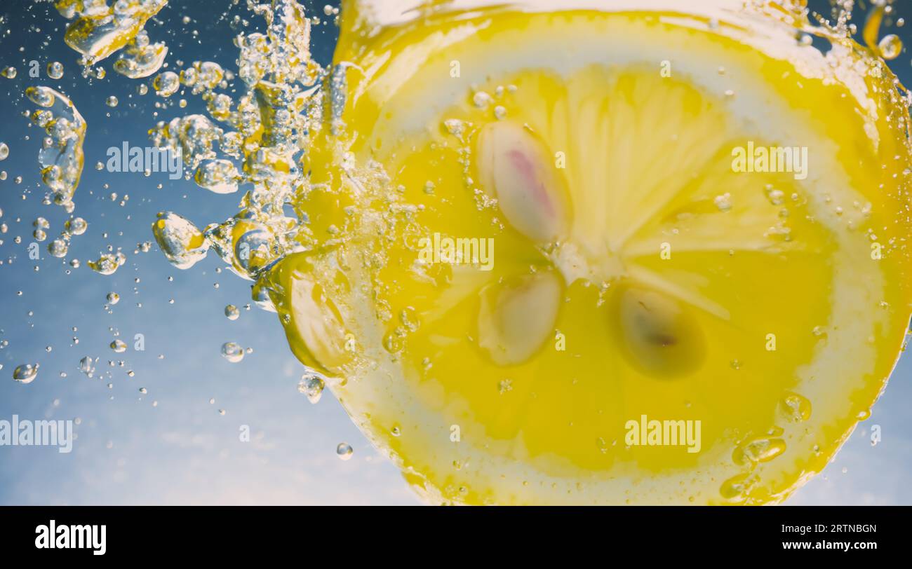 Tranche de citron sous-marine dans de l'eau gazeuse ou de la limonade avec des bulles. Cocktail rafraîchissant soda tonique pétillant. Gros plan de citrons et de glaçons en verre. Lime i. Banque D'Images