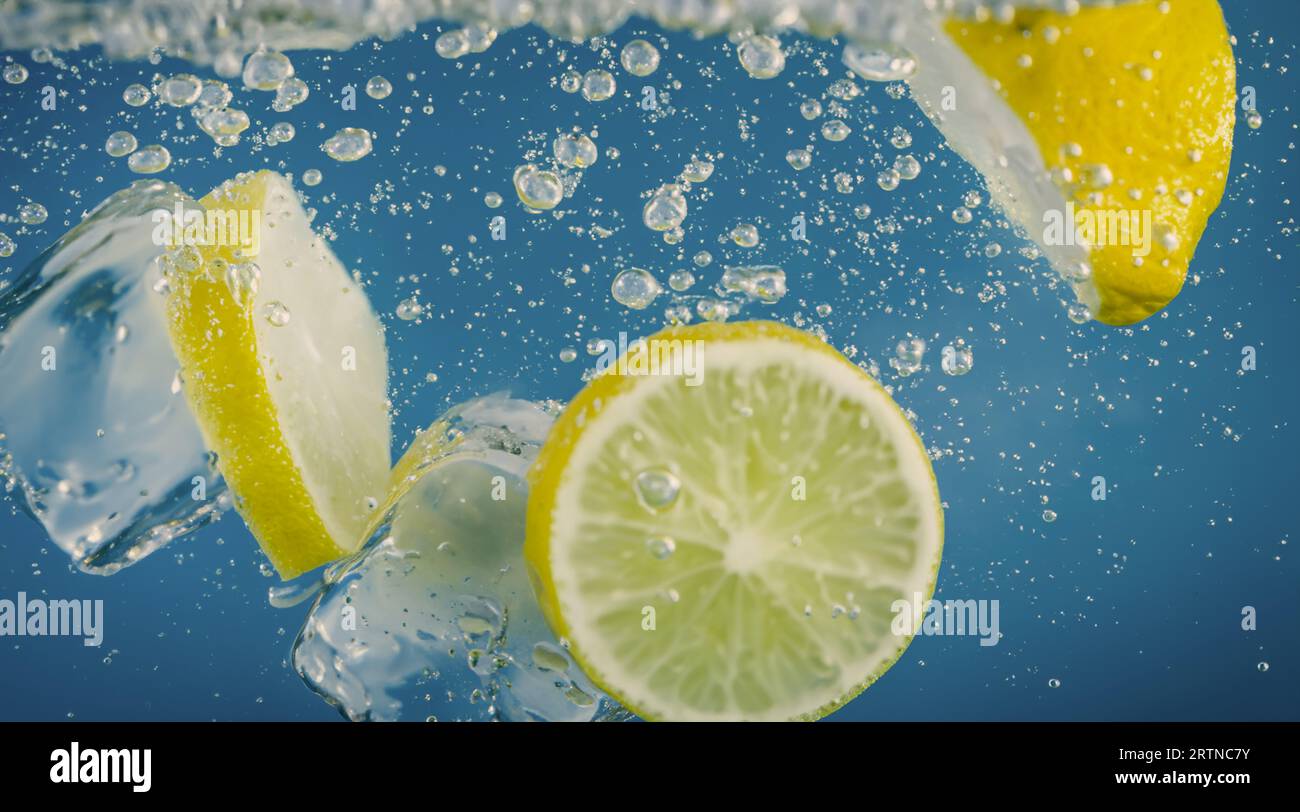 Tranche de citron sous-marine dans de l'eau gazeuse ou de la limonade avec des bulles. Cocktail rafraîchissant soda tonique pétillant. Gros plan de citrons et de glaçons en verre. Lime i. Banque D'Images