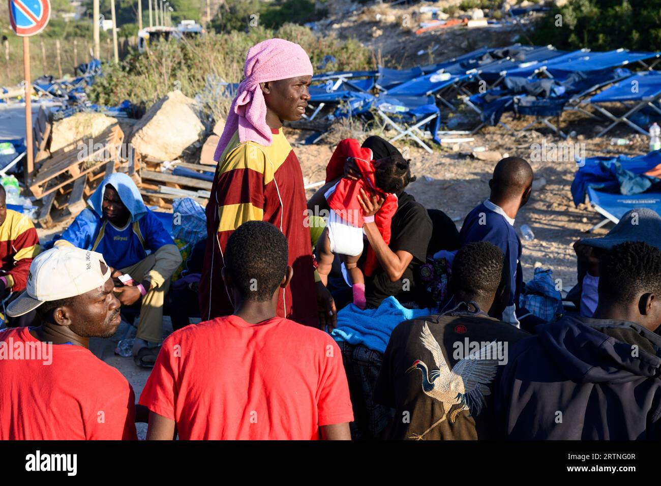 Migrants sit outside the Lampedusa's migrant reception center, Sicily, Thursday, Sept.14, 2023. The reception center in Italy's southernmost island of Lampedusa remained critical Thursday as it coped with transferring to the mainland thousands of migrants who arrived on small, unseaworthy boats in a 24-hour span this week. (AP Photo/Valeria Ferraro) Banque D'Images