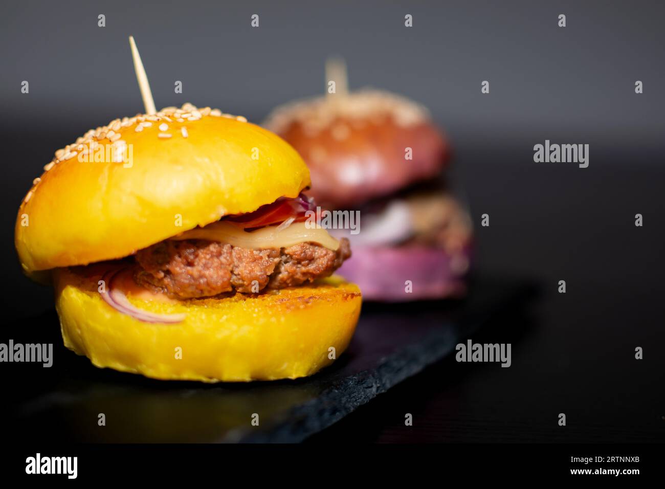 Mini Burgers Gourmet colorés avec des graines de sésame sur planche d'ardoise noire Banque D'Images