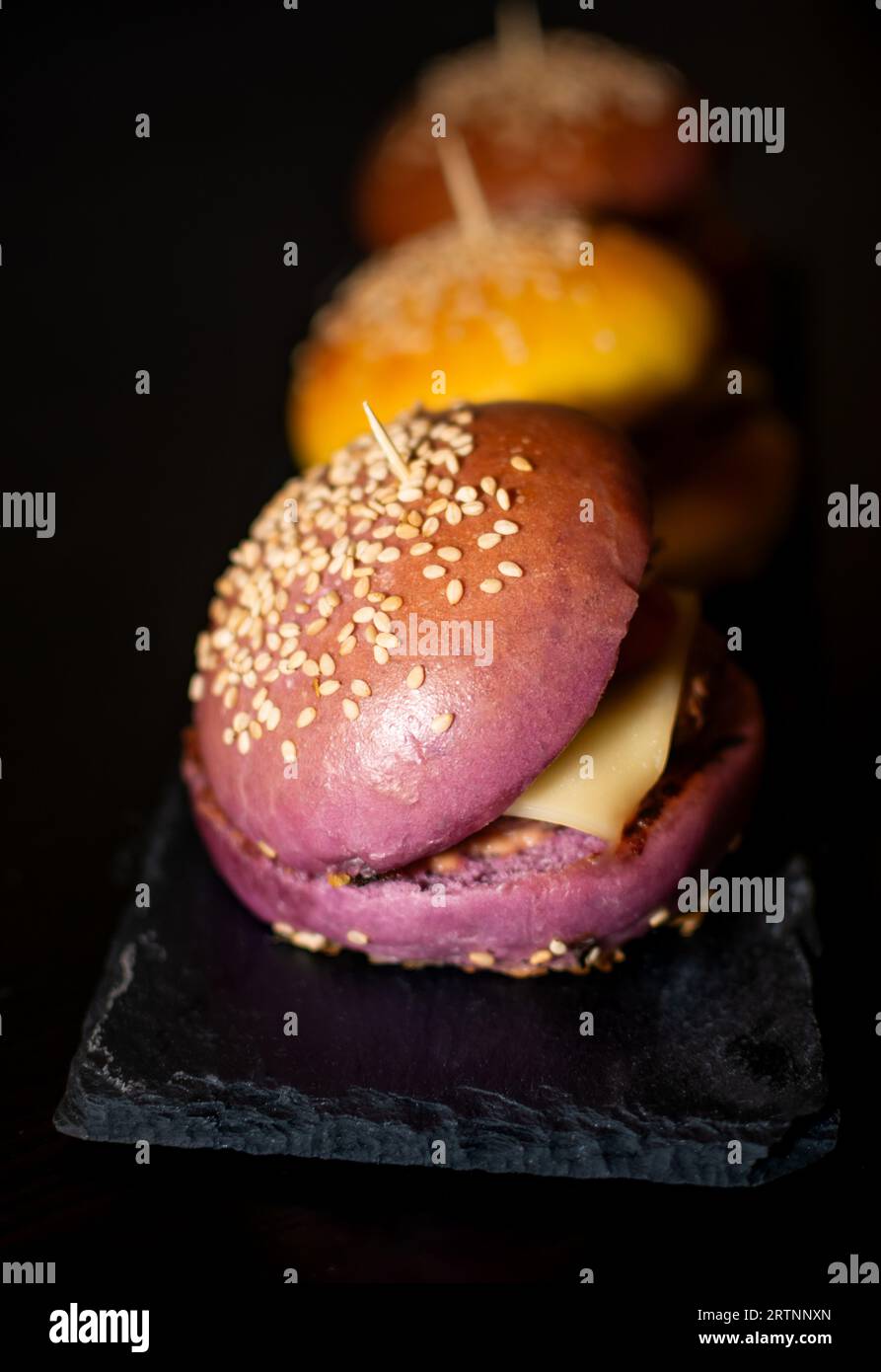 Mini Burgers Gourmet colorés avec des graines de sésame sur planche d'ardoise noire Banque D'Images