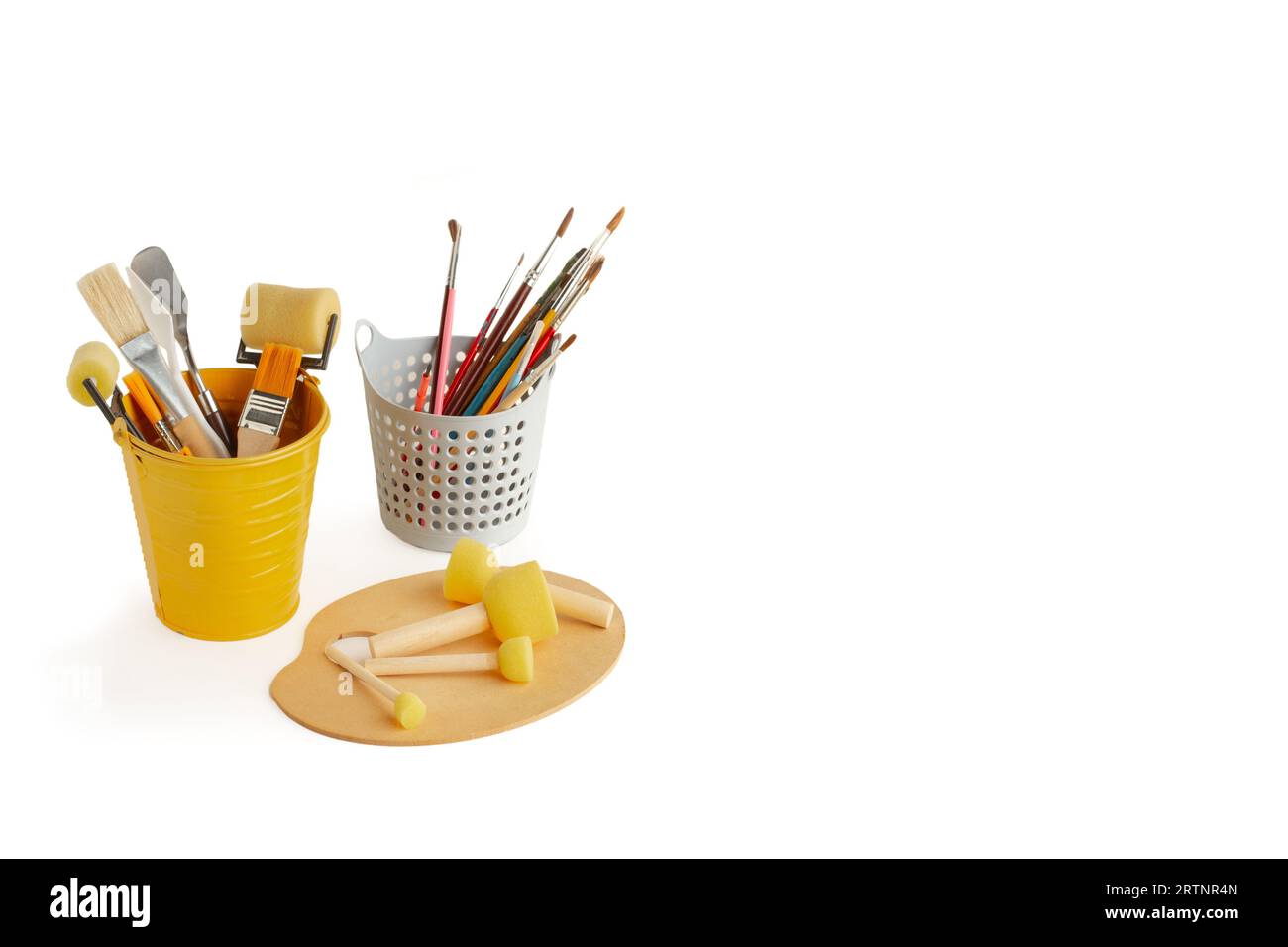 Pinceaux, rouleaux et spatules dans des seaux et brosse mousse éponge ronde sur une palette en bois sur fond blanc Banque D'Images