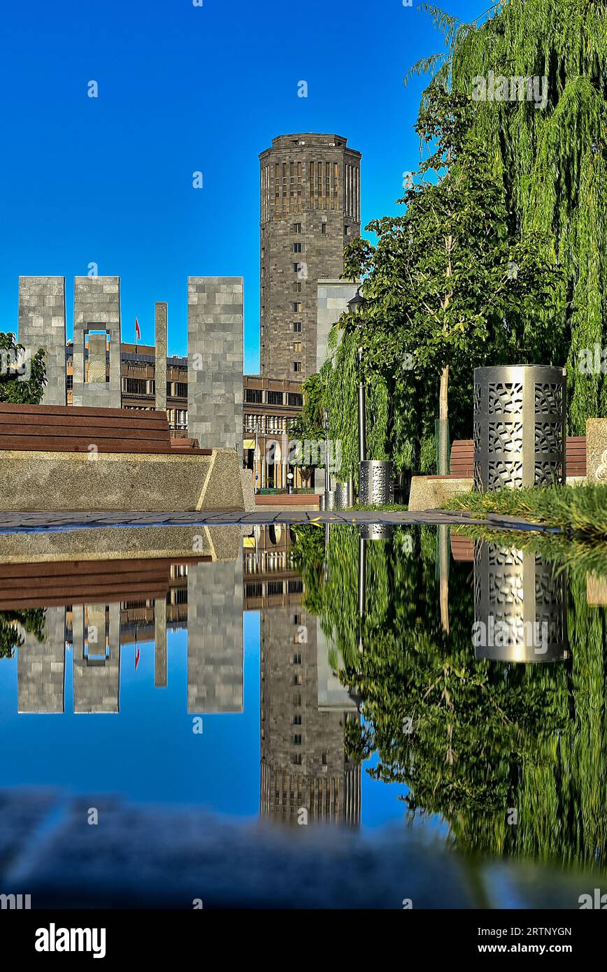 Alexander Myasnikyan Square, l'usine de brandy arménien Noy, et leur reflet dans une flaque d'eau, du parc Vardanyan/parc du 2800e anniversaire d'Erevan Banque D'Images