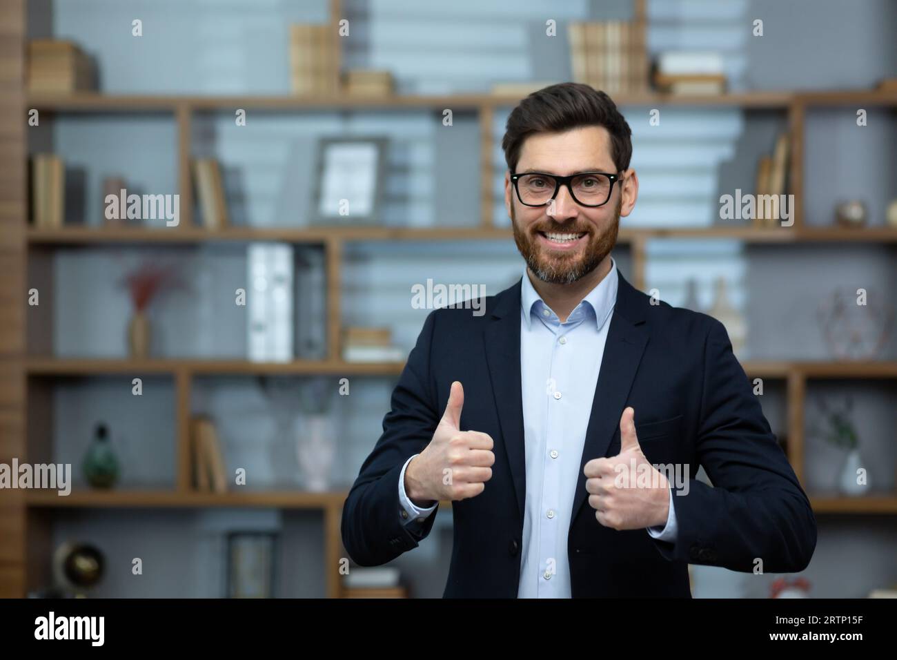 Portrait d'un financier réussi à l'intérieur du bureau, l'homme sourit et regarde la caméra, montrant un pouce positif vers le haut, Banque D'Images