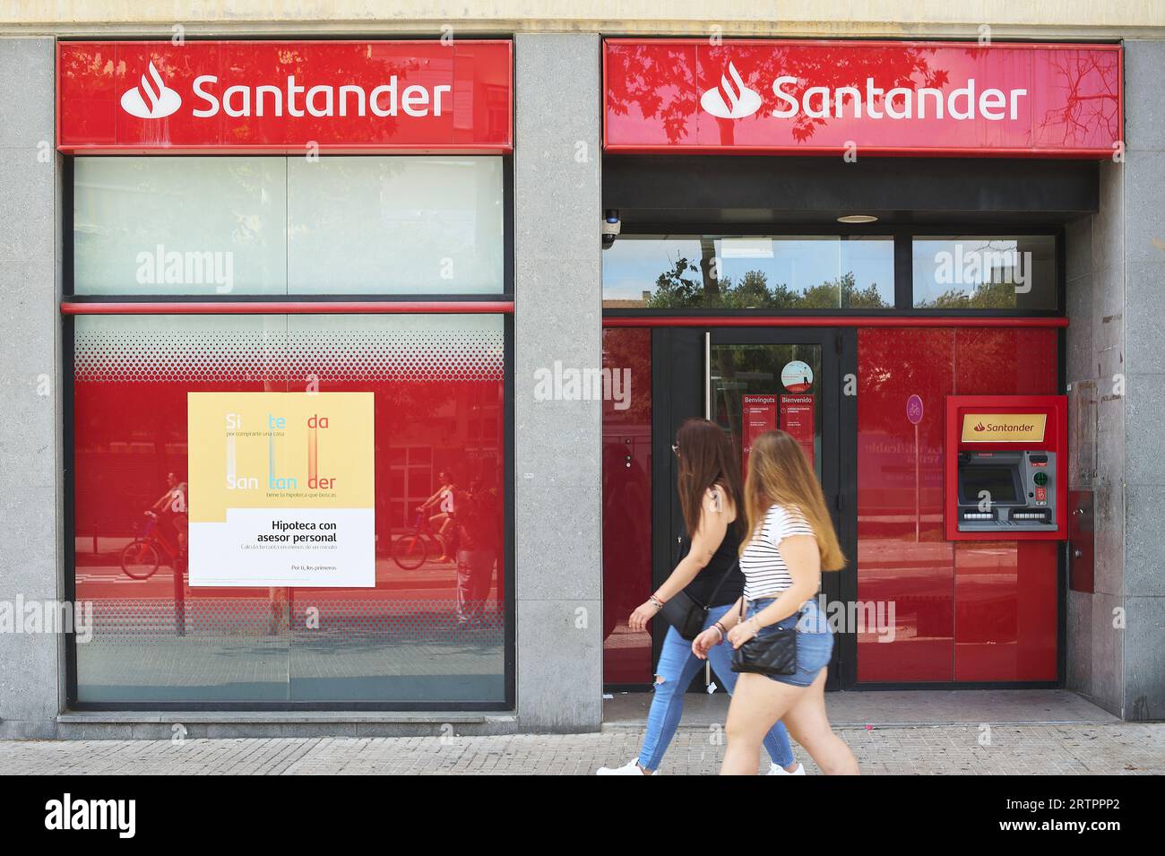 Viladecans, Espagne - 12 septembre 2023 : deux jeunes femmes méconnaissables passant et regardant une succursale de la banque Santader par une journée ensoleillée. Banque D'Images