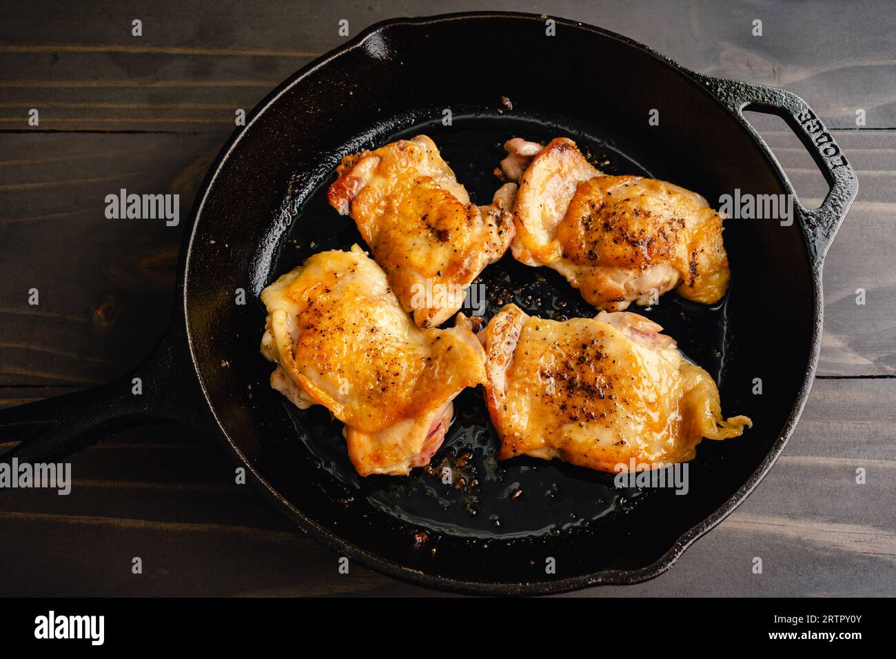 Cuisses de poulet saisies dans une poêle en fonte : quatre cuisses de poulet poêlées avec peau dans une poêle, placées sur une table en bois Banque D'Images