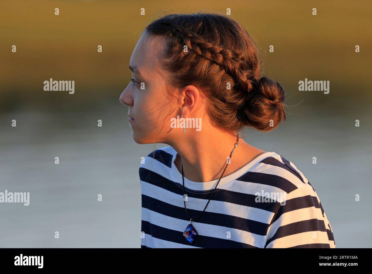 Beau portrait de profil de fille adolescente au coucher du soleil isolé sur fond orange et gris Banque D'Images