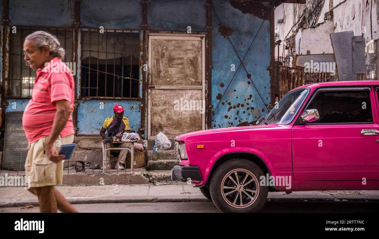 La Havane, Cuba le 23 décembre 2015 : un homme marche dans une rue dans le centre de La Havane avec sa chemise assortie à la couleur d'un oldtimer rose Banque D'Images