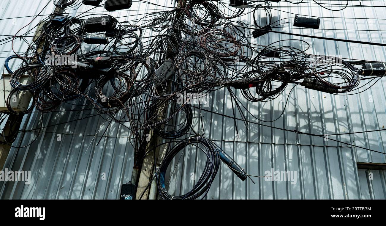 Les fils électriques emmêlés et les lignes de communication emmêlées sur les poteaux électriques urbains créent un réseau chaotique. Désorganisé et désordonné à l'organisation Banque D'Images