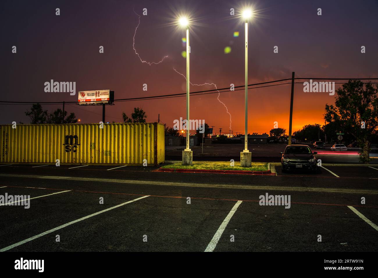 La foudre frappe à l'heure magique au-delà d'un parking aléatoire avec un conteneur d'expédition jaune vif alors que le jour se transforme en nuit à Amarillo, Texas. Banque D'Images