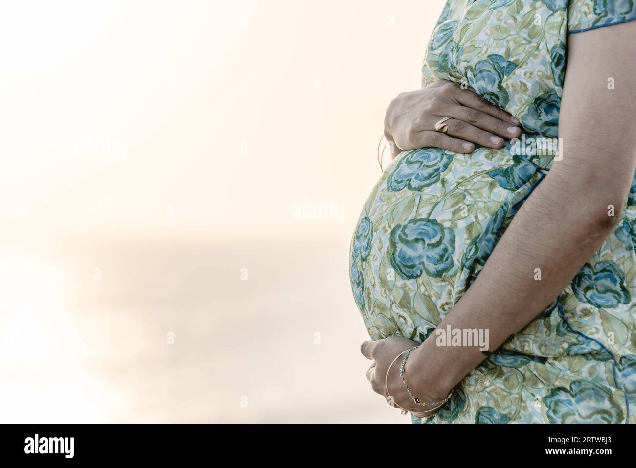 Young pregnant woman holding her belly avec coucher du soleil derrière elle Banque D'Images