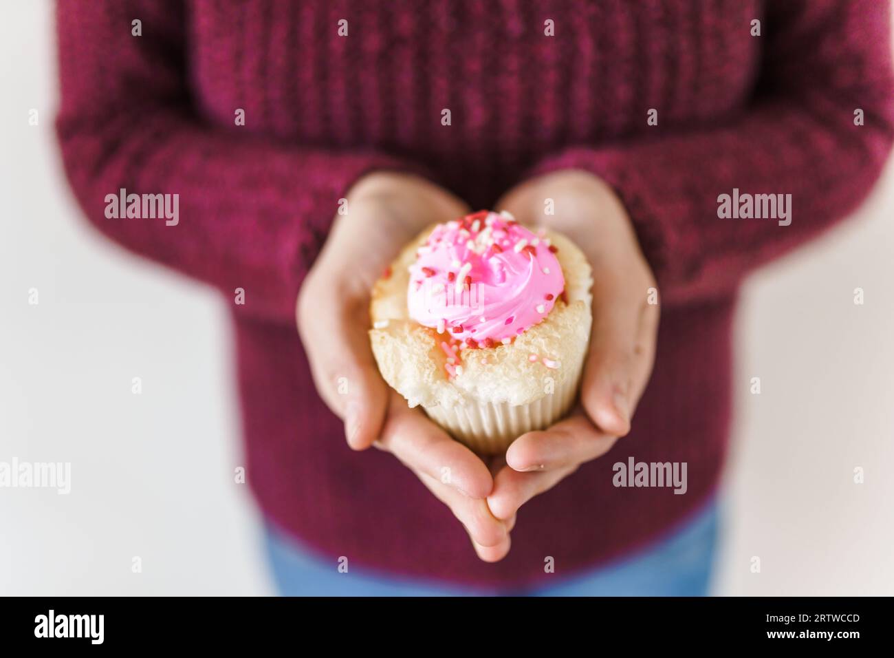 Une femme dans un pull rose tenant un cupcake avec du glaçage rose Banque D'Images