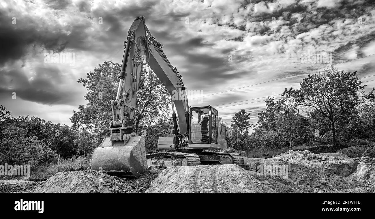 Pelle sur chenilles pendant les travaux de terrassement sur le chantier en vue bannière noir et blanc Banque D'Images