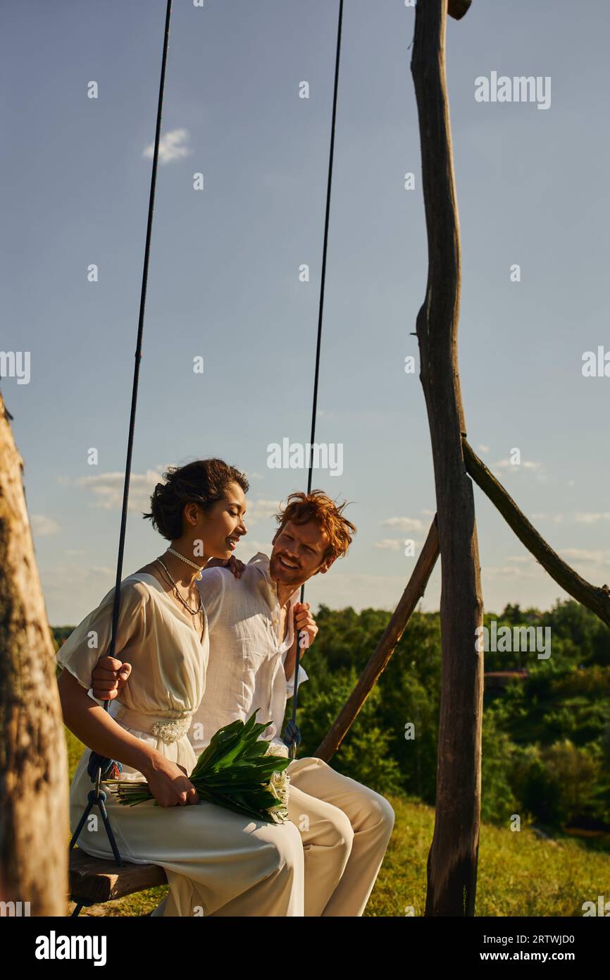 jeune mariée asiatique avec des fleurs balançant avec le marié rousse insouciant, mariage dans la campagne tranquille Banque D'Images