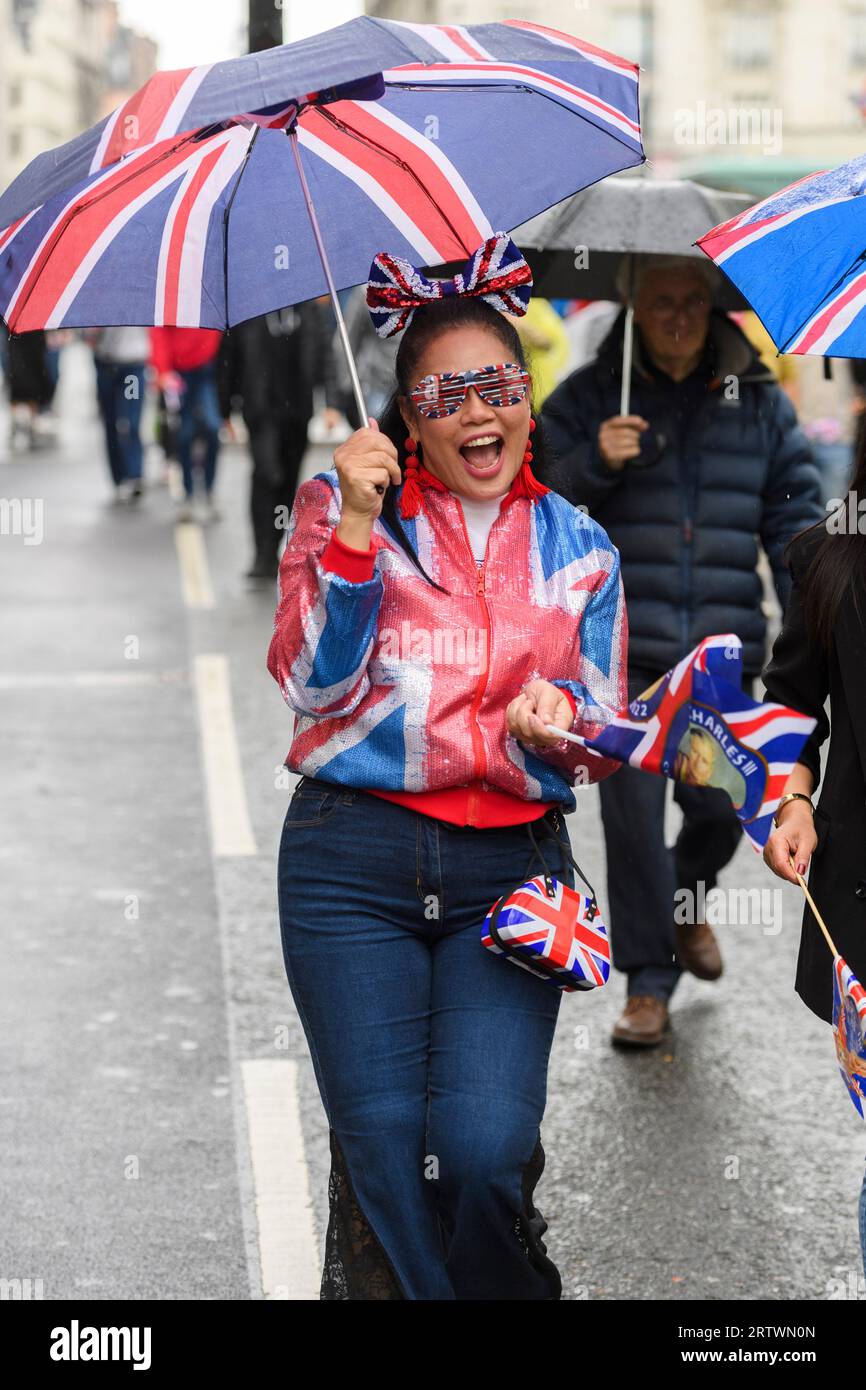 Une femme, vêtue d'une veste Union Jack, et des lunettes, et portant un parapluie et un sac assortis, descend un Piccadilly pluvieux, partie d'une grande foule h Banque D'Images