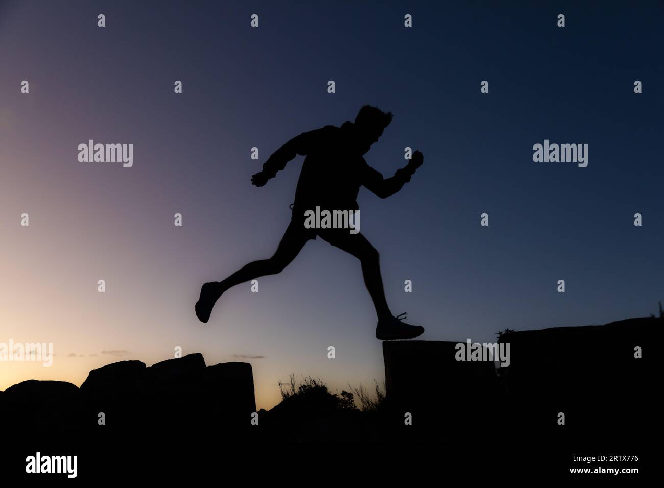 Jeune homme sur une randonnée prenant une longue foulée au lever du soleil en silhouette Banque D'Images