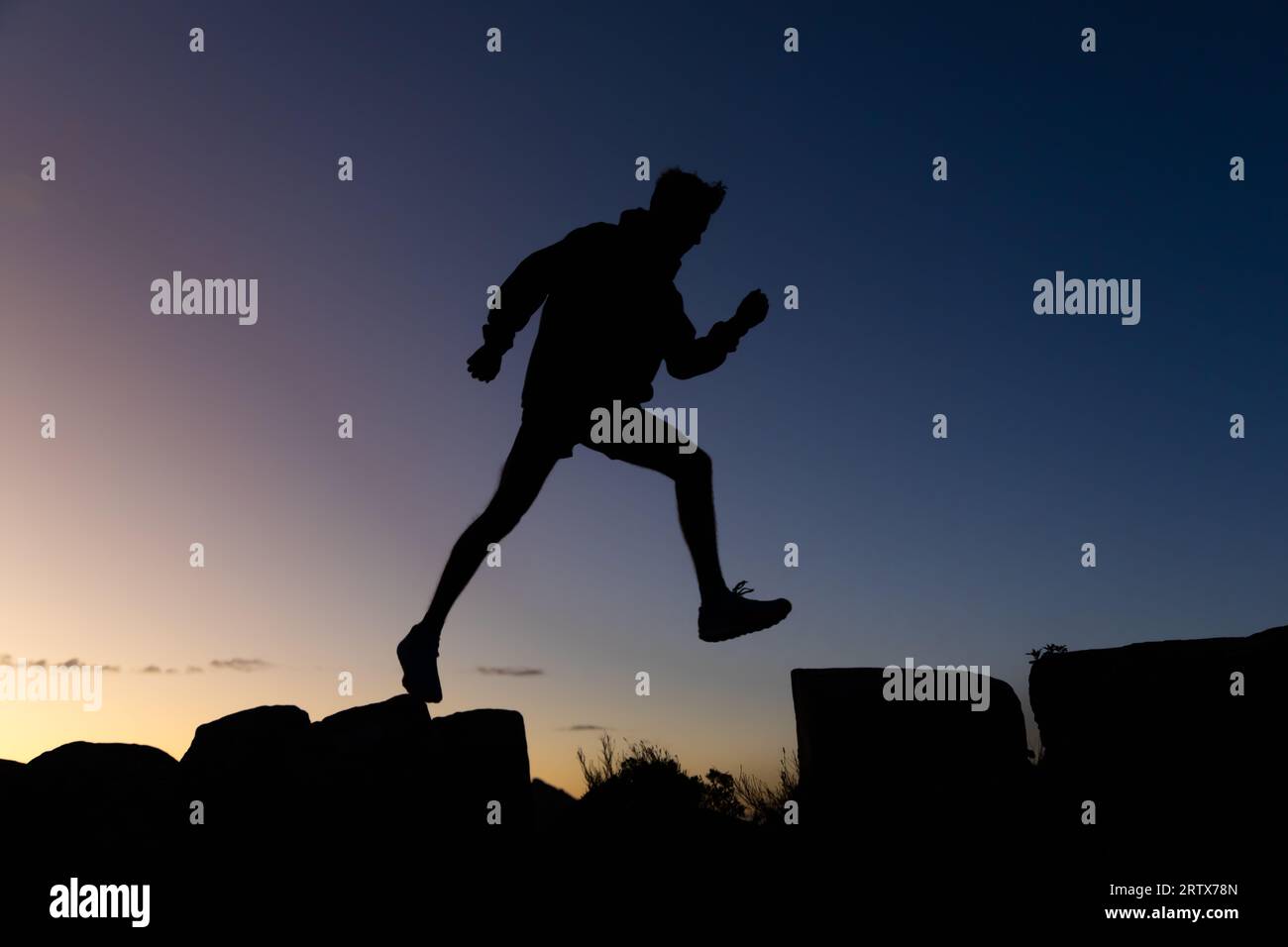 Jeune homme sur une randonnée prenant une longue foulée au lever du soleil en silhouette Banque D'Images