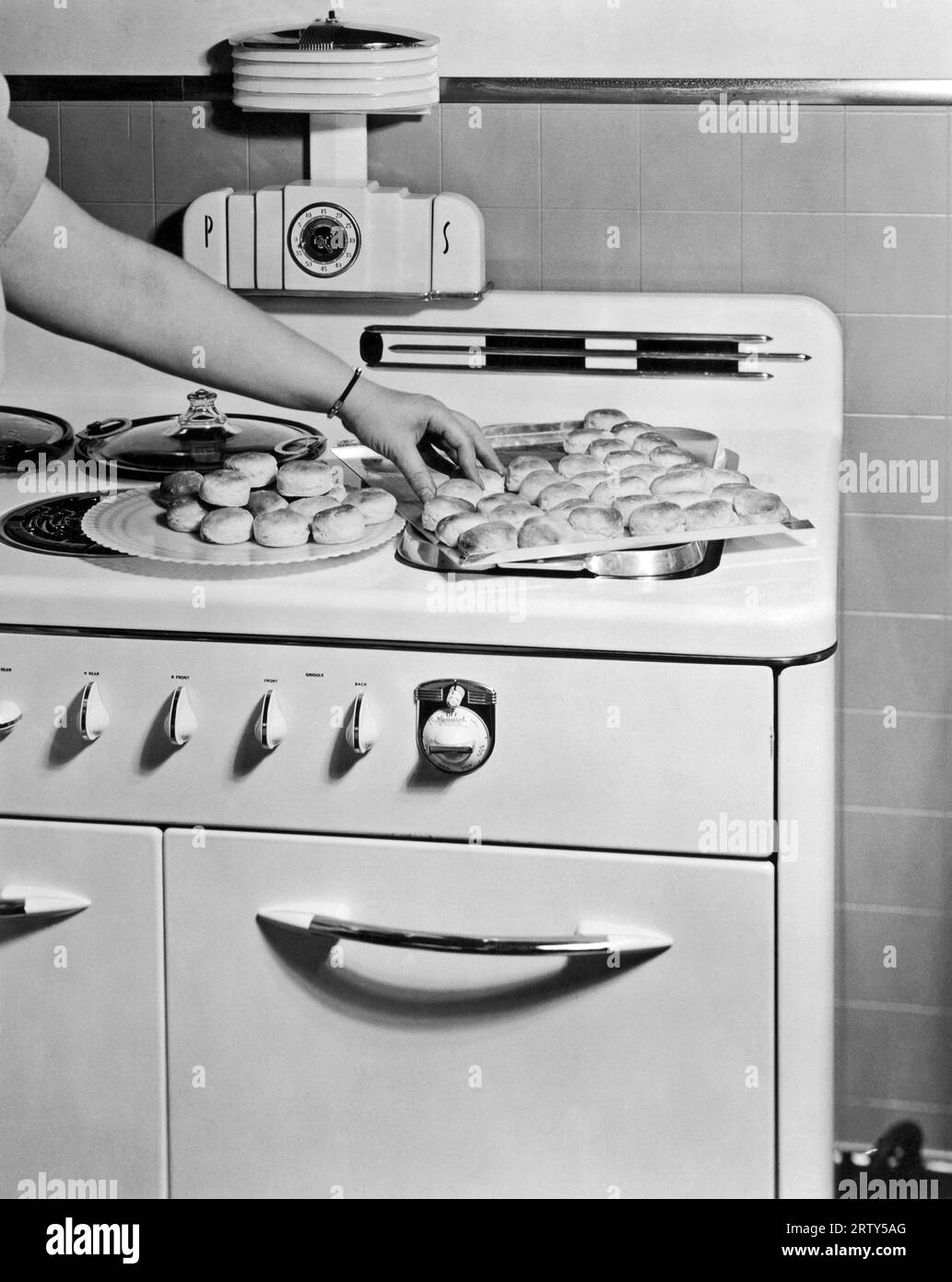 Wisconsin c 1935. Une femme transfère des biscuits fraîchement cuits dans son poêle Monarch sur une assiette de la plaque à biscuits. Banque D'Images