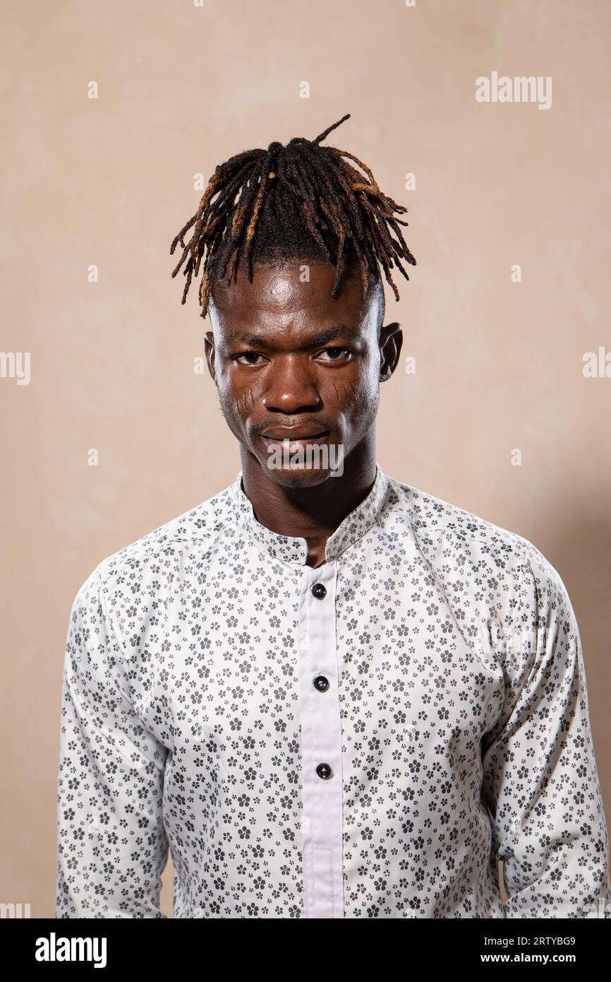 Portrait d'un jeune homme africain avec des dreadlocks et élégamment vêtu d'une chemise blanche. Expression sérieuse et regardez la caméra Banque D'Images