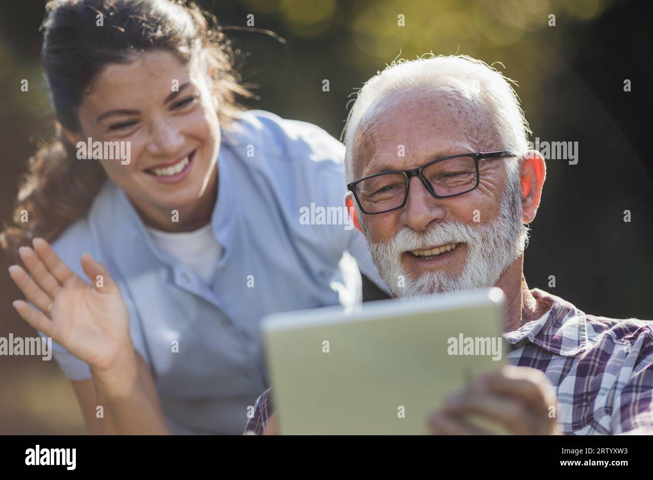 Homme âgé et jeune femme soignant utilisant la tablette pour appel vidéo en plein air dans le parc Banque D'Images