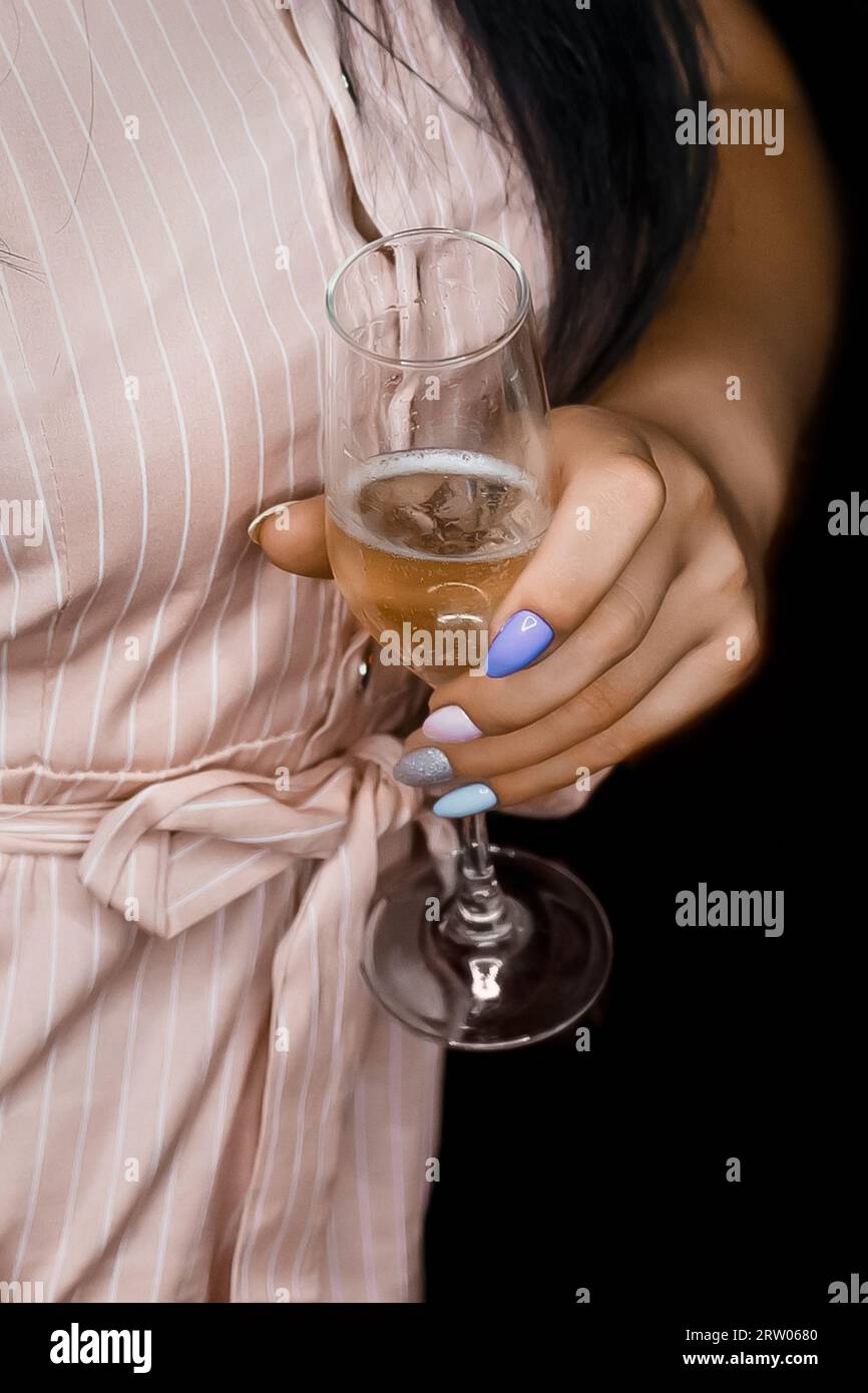 Main d'une jeune fille tenant un verre d'alcool léger, champagne frais, gros plan sur le fond noir. Banque D'Images