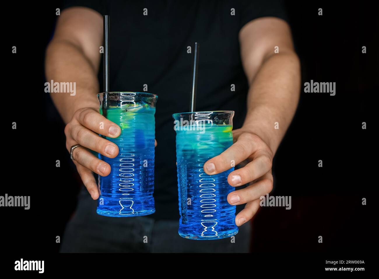 Les mains du barman servent 2 cocktails alcoolisés au sirop bleu lagon sur fond noir. Banque D'Images
