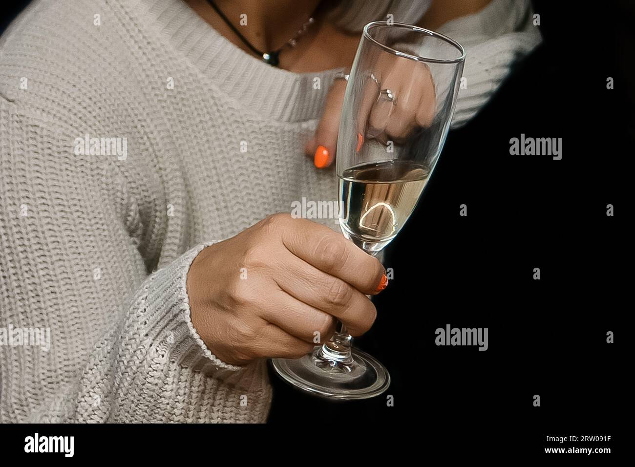 Gros plan de la main d'une femme adulte tenant un verre d'alcool de champagne mousseux frais sur un fond noir. Banque D'Images