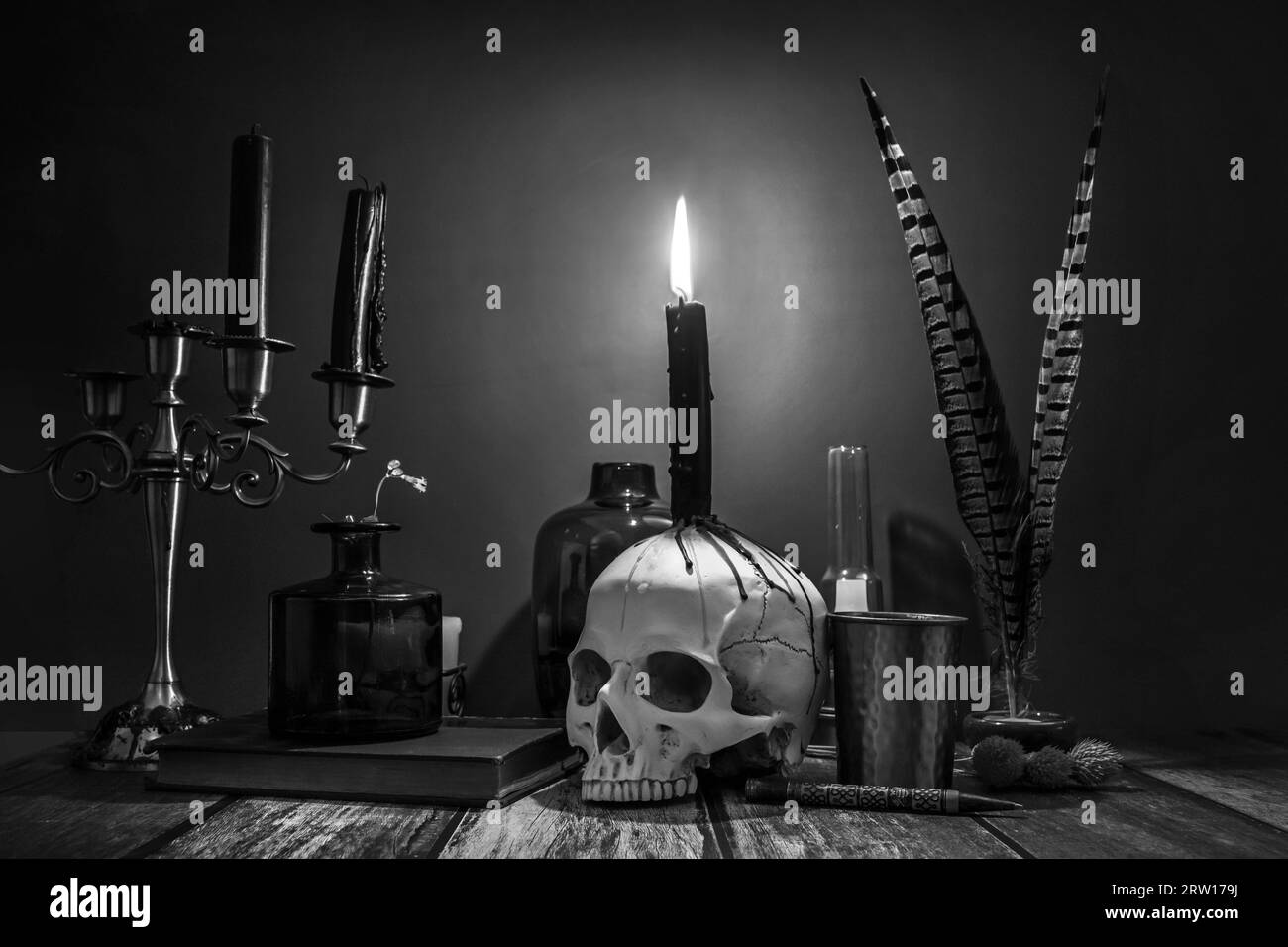 Une image en noir et blanc de bougies dans un candélabre, un crâne avec des gouttes de cire et des objets vintage pour scribes Banque D'Images