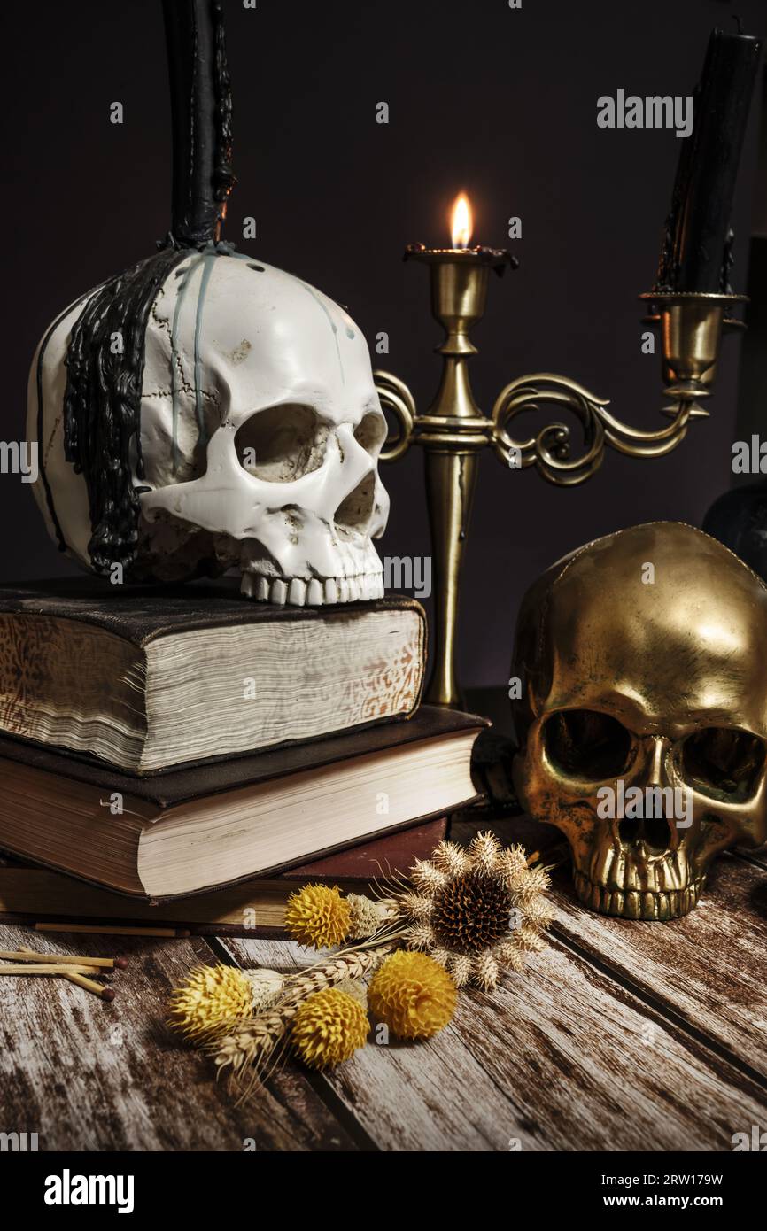 Nature morte de style gothique avec des fleurs séchées, des crânes humains, de vieux livres, un chandelier avec des bougies allumées sur une table en bois Banque D'Images
