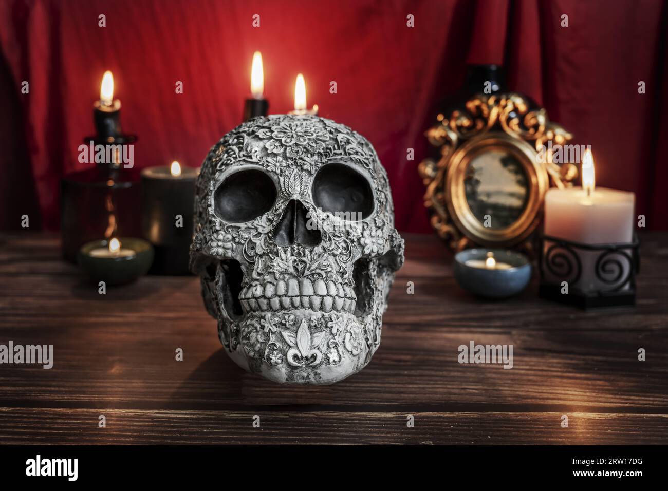 Une nature morte de style gothique avec un crâne décoré, des bougies allumées et un tissu rouge cramoisi Banque D'Images