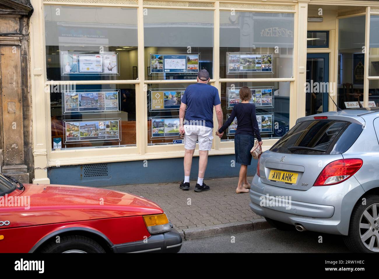 Personnes regardant des maisons à vendre dans une vitrine d'agents immobiliers le 13 septembre 2023 à Cirencester, Royaume-Uni. Cirencester est connu pour avoir un grand nombre d'agents immobiliers dans son petit centre-ville car le marché du logement rural reste actif. Cirencester est une ville de marché dans le Gloucestershire. C'est la huitième plus grande colonie du Gloucestershire et la plus grande ville des Cotswolds. La plupart des bâtiments et des maisons de la ville sont fabriqués à partir de la pierre de Cotswold de couleur miel distinctive. Banque D'Images