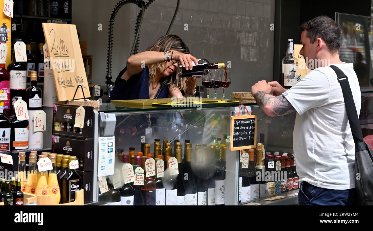 Les femmes versent un verre de vin comme échantillon de dégustation pour l'homme dans l'étal de marché vendant des bouteilles de vin Banque D'Images