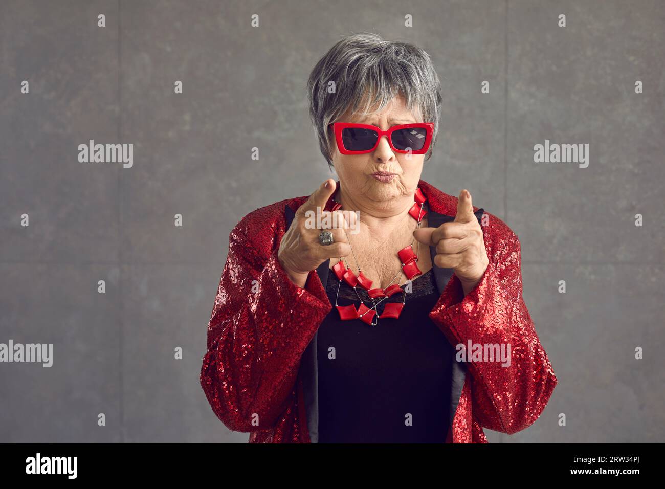 Femme senior en veste disco fait un visage drôle et pointe ses index à la caméra Banque D'Images