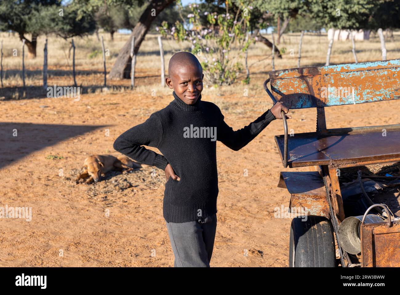 jeune enfant africain de village avec la tête chauve debout à l'extérieur à côté d'un chariot d'âne Banque D'Images