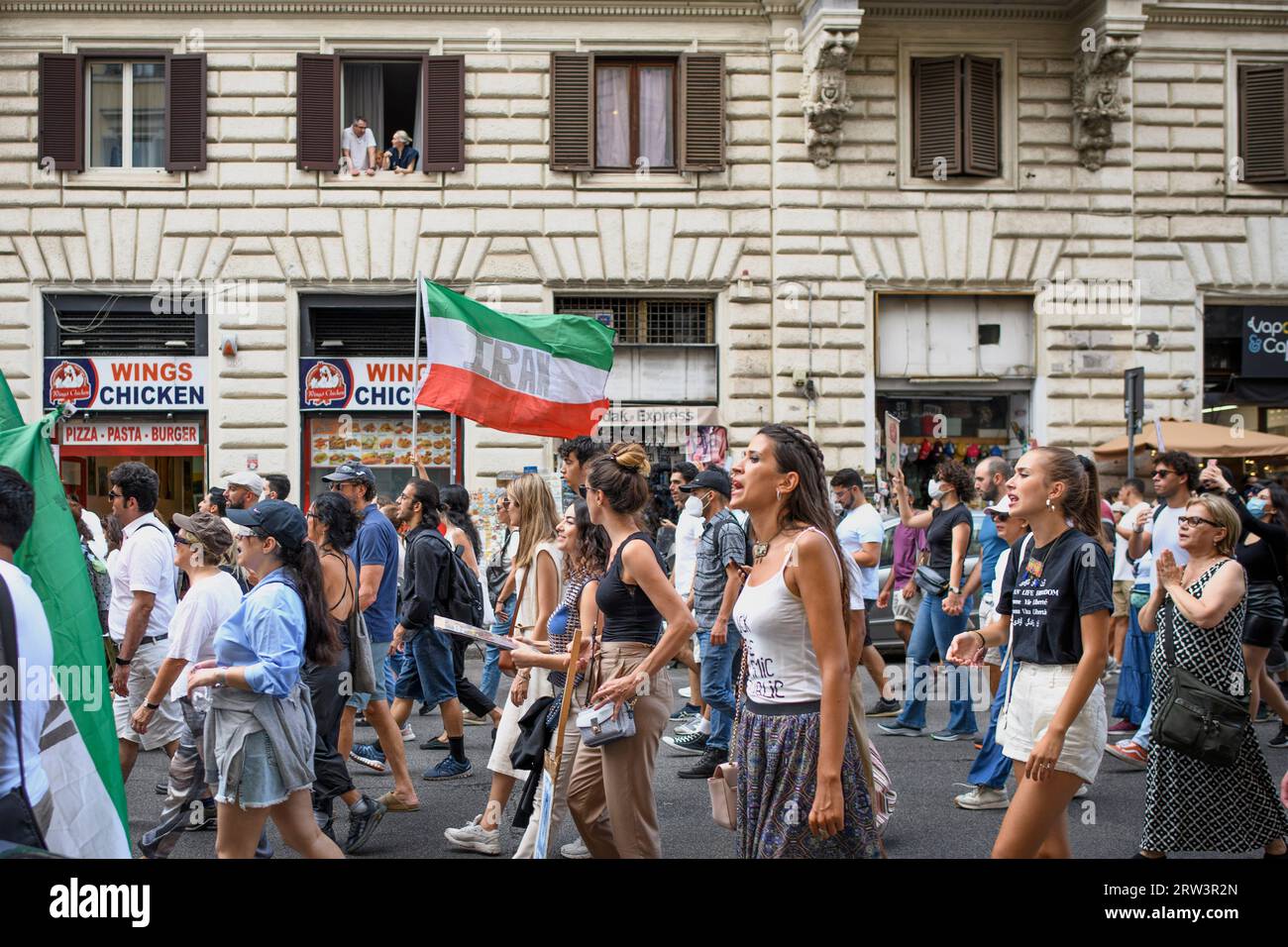 Rome, Italie. 16 septembre 2023. 16 septembre 2023, Rome, Italie : deux spectateurs regardent depuis la fenêtre des femmes qui protestent contre le régime iranien autour du drapeau iranien lors de la manifestation commémorant la mort de Mahsa Amini à Rome. Mahsa Amini, arrêté à Téhéran le 13 septembre 2022 par la police religieuse pour non-respect de la loi sur le port obligatoire du voile. Elle est décédée dans des circonstances suspectes après trois jours dans le coma le 16 septembre 2022 à l'âge de 22 ans. Crédit : ZUMA Press, Inc./Alamy Live News Banque D'Images