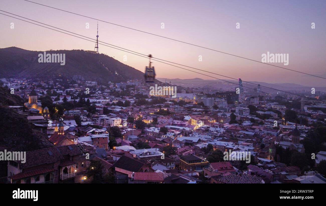 Drone point de vue en soirée illuminé Tbilissi. Églises et vieille ville et Tour de communication sur hil dans la capitale géorgienne. Téléphérique mobile. Iconi Banque D'Images