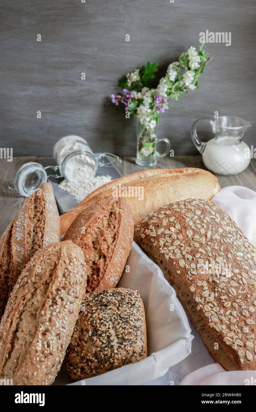 Miches et miches de pain artisanal rustique fait avec différents types de graines et farines, avec un pot de lait et un pot de farine sur blanc et rose Banque D'Images